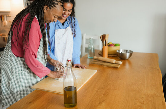 Happy african mother and daughter preparing together bread at home during winter holidays - Family women having fun cooking together - Main focus on mum face