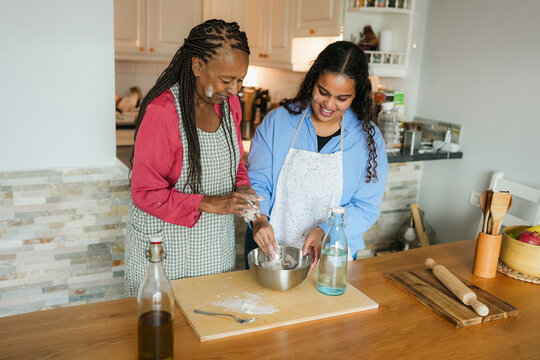 Happy african mother and daughter preparing together bread at home during winter holidays - Family women having fun cooking together - Main focus on girl face