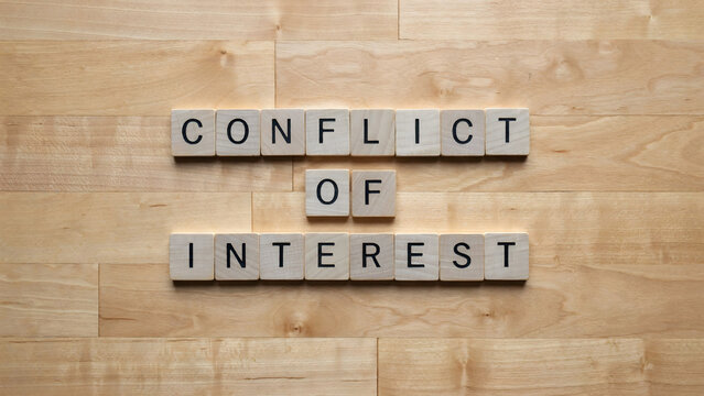 Conflict of interest text spelled out with wooden tiles on a wooden background