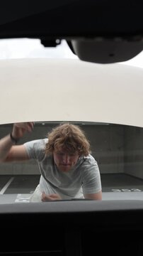Vertical screen focused car owner starts fixing the vehicle himself with a screwdriver under the open hood attempting a practical do it yourself repair without a mechanic