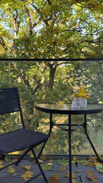 White skull planter filled with maple leaves stands on balcony table surrounded by autumn trees. Halloween balcony styling, small space seasonal decor, gothic autumn aesthetic, foraged leaf decorating