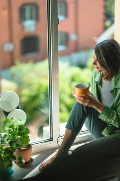 Person relaxing with mug while robot cleans window indoors