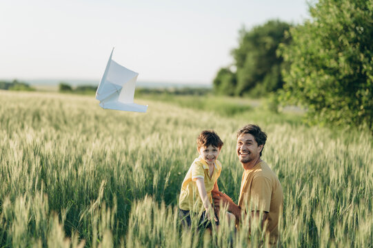 Father and son launch a paper airplane in a summer field