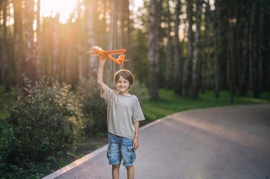 A smiling boy walks in the park at sunset launching a toy airplane