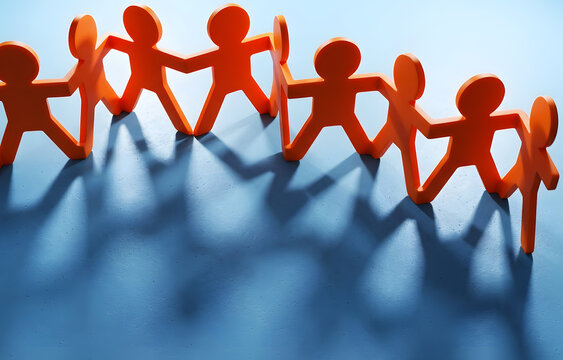 Orange paper cutout figures holding hands in a chain with strong shadows on a blue background, symbolizing teamwork and unity.