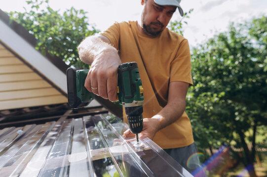 A man repairs a plastic roof with a drill outdoors