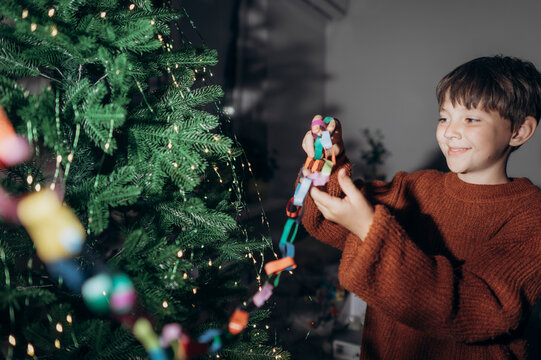 Smiling boy decorates a Christmas tree with a paper garland at home