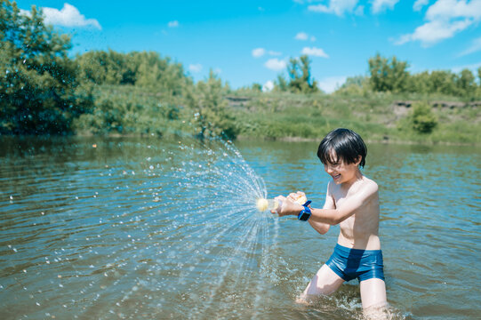 Smiling boy shoots water from a toy in the river