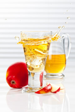 Carafe and glass with splashing apple juice, close up