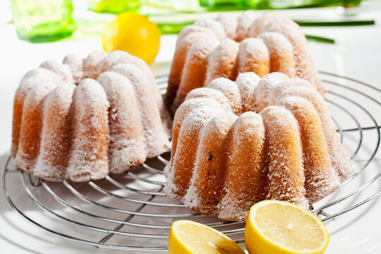 Lemon cake with icing sugar and lemons on cooling rack, close up