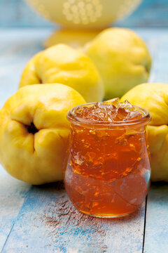 Four quinces (Cydonia oblonga), a spoon and a glass of quince marmalade on wooden table