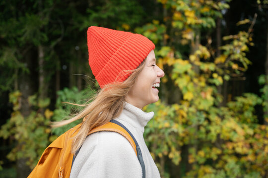 A smiling woman wearing a backpack hikes through an autumn forest