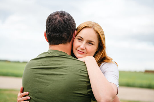 A smiling woman embraces a man outdoors in the countryside