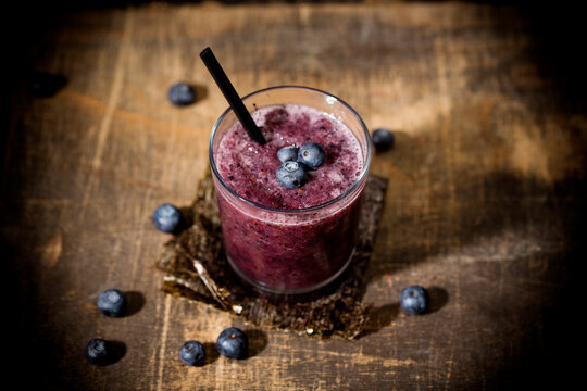 Glass of blueberry smoothie and blueberries on wooden table