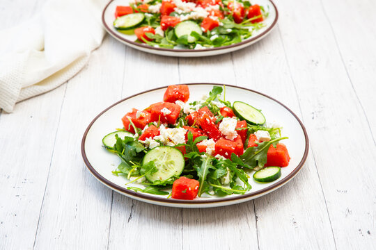 Fresh watermelon salad with feta and arugula sits on a wooden table