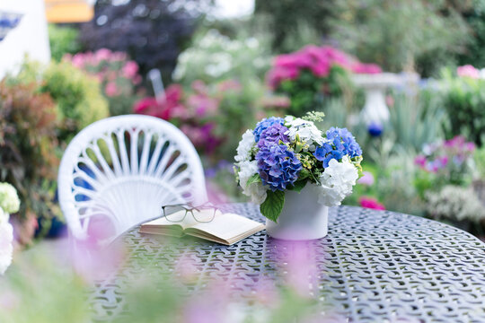 A metal table holds a book and a hydrangea bouquet in a garden