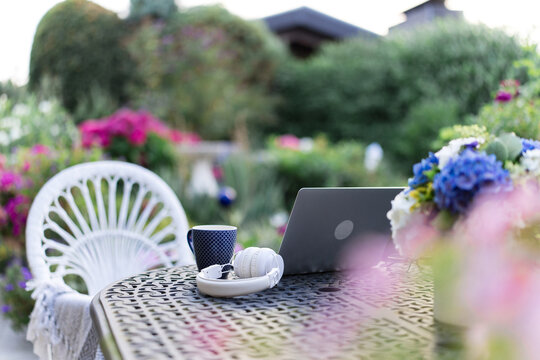 A laptop and headphone sit on a garden table for remote work