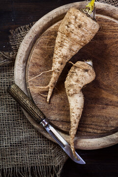 Two parsley roots and peeler on wooden board
