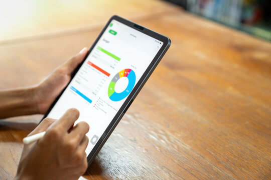 A businessman hands holding tablet device and writing notes on financial budget planner template over a wooden table surface.