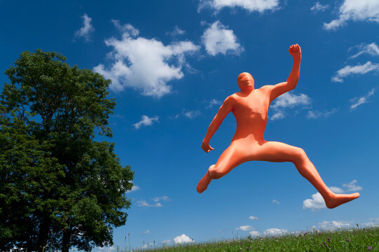 Germany, Bavaria, Man in orange zentai jumping in landscape