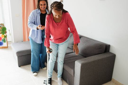 African american daughter helping her mother walk with foot brace after a surgical operation - Medical, insurance and health care concept - Main focus on mum face - UGC content