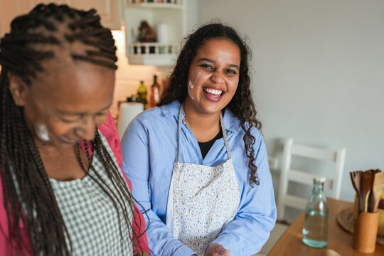 Happy african mother and daughter preparing together bread at home during autumn holidays - Family women having fun cooking together - Main focus on girl face - UGC wide lens content