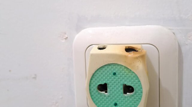 Close-up of a dangerous burnt electric socket adapter plugged into a wall outlet. Electrical hazard, short circuit safety hazard, and risk stock photo.