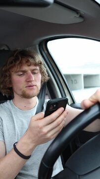 Vertical screen driver compulsively checks social media on a smartphone behind the wheel revealing dangerous phone addiction while the car continues through urban traffic