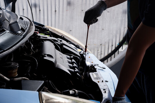 Mechanic pulling out oil dipstick to check motor engine oil level and condition in car compartment.