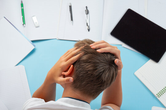 student holding head stressed with homework assignments overwhelmed young boy top view blue background with notebooks and tablet with copy space for banner design, education difficulty psychology
