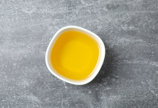 Bowl of fresh oil on grey background