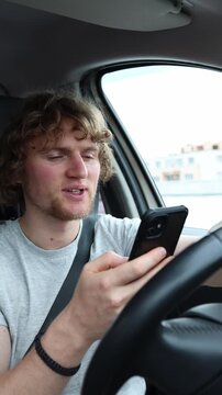 Vertical screen inattentive driver scrolls through social media on a smartphone behind the wheel while the car moves through traffic creating a serious road safety hazard