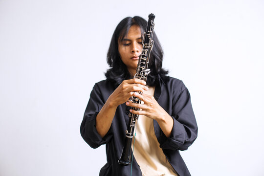 Young Asian Man with Long Hair Holding and Adjusting an Oboe Woodwind Instrument
