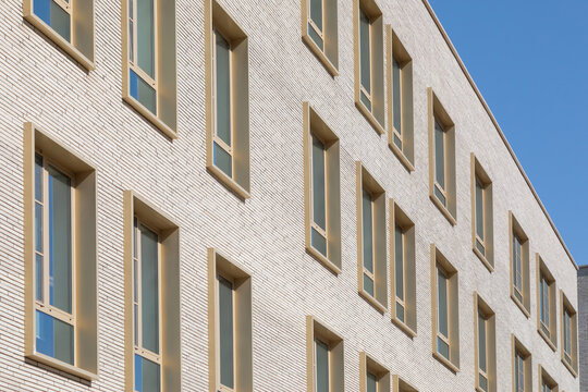 Modern beige brick building facade with rows of rectangular windows against blue sky. Real Photo.