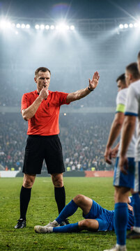 Referee stops play near injured footballer and signals toward players. Concept of player safety, injury response and match control.