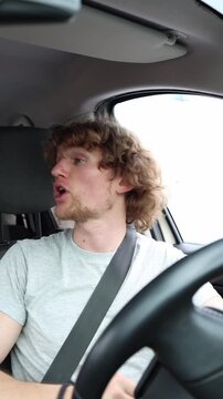 Vertical screen angry young man shouts at nearby drivers from his sedan expressing road rage and frustration while stuck in heavy traffic during a stressful urban commute
