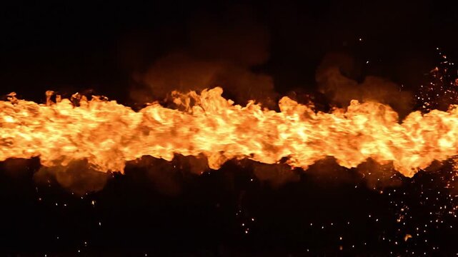 Horizontal stream of intense fire flame jet with sparks on black background. Continuous flamethrower blaze motion for energy, danger and power concept