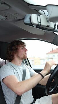 Vertical screen worried beginner drives through the city with both hands on the wheel feeling anxious and overwhelmed because he lacks experience and basic driving skills
