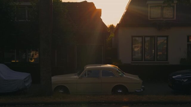 Vintage classic oldtimer car parked in front of a historic Dutch house, beautifully illuminated by warm golden backlight during a picturesque sunset.
