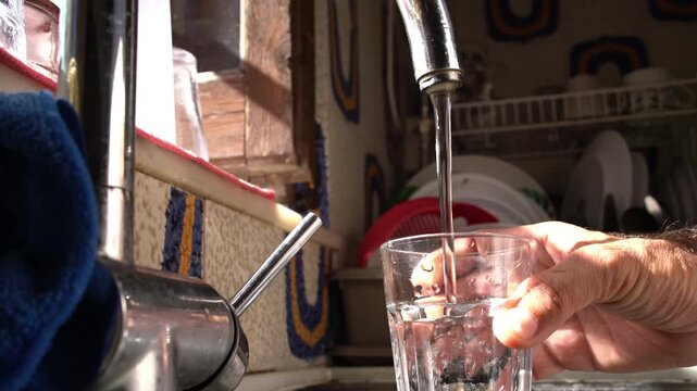 A hand holds a glass and fills it with water from a kitchen faucet, Close-up Shot