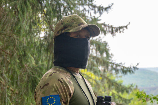 Masked man in camouflage stands outdoors with European Union patch