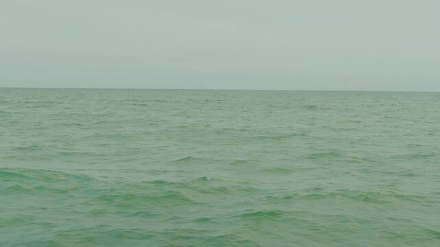 Slow-motion view from a sailboat across the wild greenish North Sea, with distant boats sailing beneath a cloudy horizon - Belgian coast, Belgium