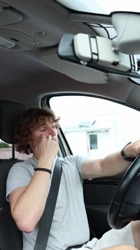 Vertical screen driver rubs painful irritated eye with one hand while continuing to drive around the city struggling with visual discomfort and controlling the moving car
