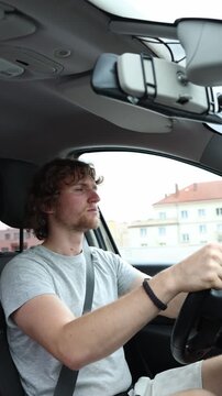 Vertical screen driver holds the steering wheel with both hands and watches the street ahead while guiding the car through a calm urban neighborhood during a daytime trip
