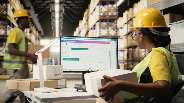 Black woman verifies barcodes and shipment details on labels and tracking software while managing supply chain logistics and e-commerce distribution.