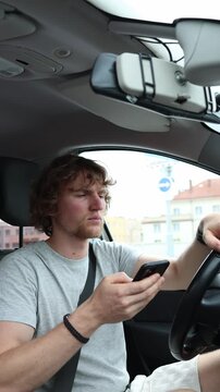 Vertical screen driver holds the steering wheel with one hand and watches his smartphone while the car moves across the city ignoring traffic and increasing accident risk