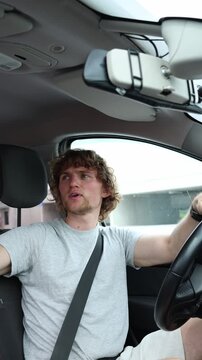 Vertical screen rude young motorist shouts insults at another driver while traveling on a busy urban road showing hostile behavior impatience and dangerous driving habits