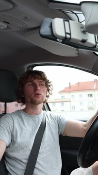 Vertical screen slightly nervous young driver travels along an urban road wearing a seat belt and glances aside while carefully controlling the moving car during his trip
