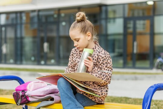 Child Reading Books Outdoors with Reusable Water Bottle and Backpack