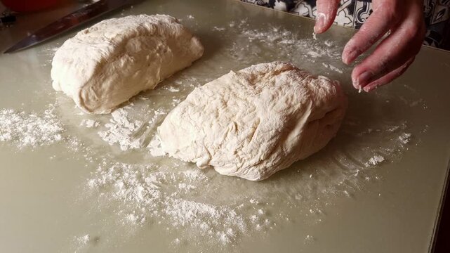 Close-up of hands working with a large ball of raw dough, dusting it with flour on a smooth kitchen counter